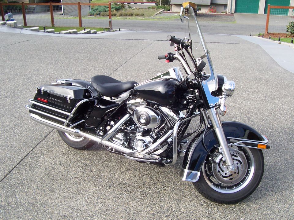 Black Harley-Davidson Road King bagger with windshield and saddlebags, front three-quarter view on concrete