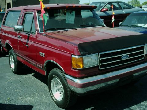 1994 Ford Bronco - This red Ford Bronco is parked outdoors, with other vehicles visible in the background.