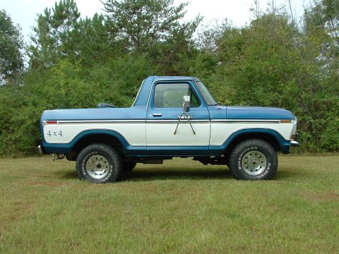 1979 Ford Bronco - Side view of a two-tone blue and white 1979 Ford Bronco parked on grass with trees in the background.