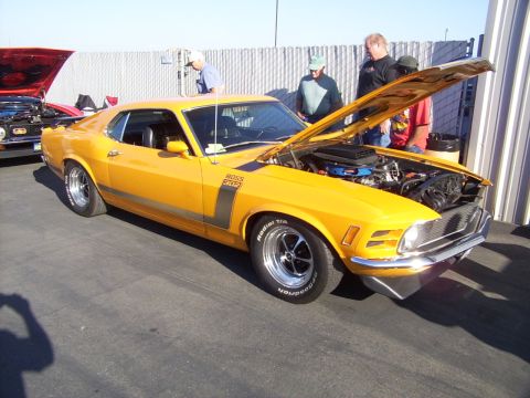 2002 Ford Mustang - A yellow 1970 Ford Mustang Boss 302 is displayed with its hood open, attracting attention from onlookers.
