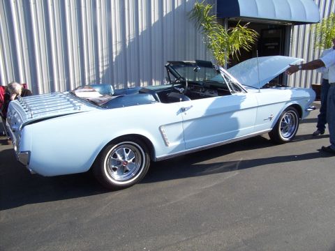 2002 Ford Mustang - A light blue 1965 Ford Mustang convertible is displayed with its hood open, parked in front of a building.