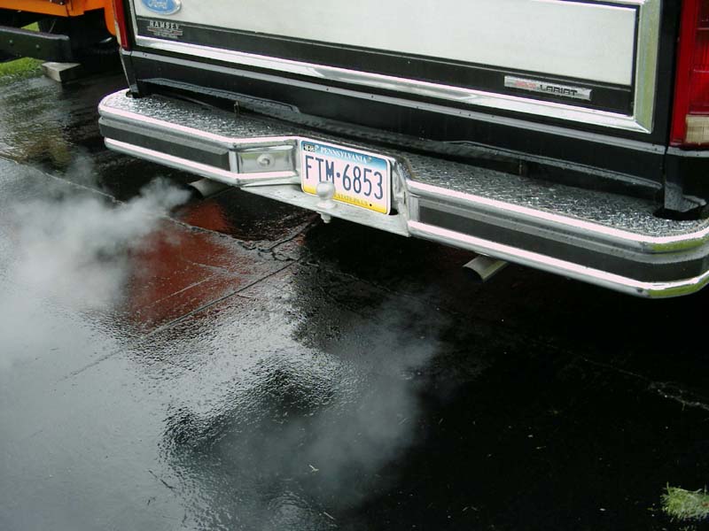 Rear of a Ford truck with smoke coming from the exhaust pipe. License plate FTM-6853 is visible