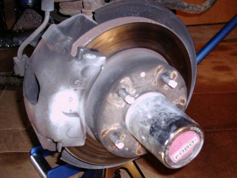 Close-up of a vehicle's front brake rotor and caliper assembly with a Ford-branded hubcap