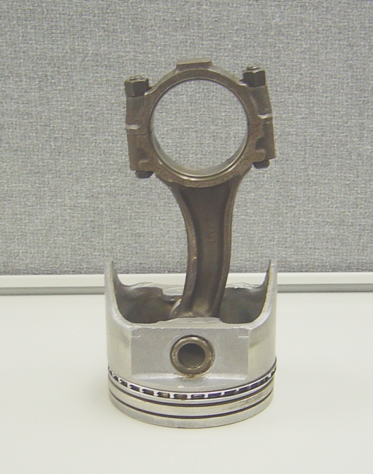 Engine piston with connecting rod attached, sitting on a white surface