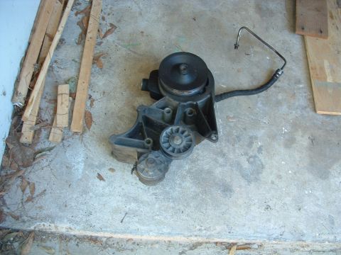 1993 Ford Bronco - This power steering pump assembly includes pulleys and a hose, shown resting on a concrete surface.