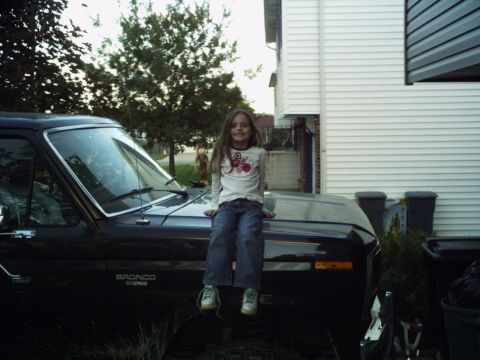 1986 Ford Bronco - A young girl sits on the hood of a black Ford Bronco.
