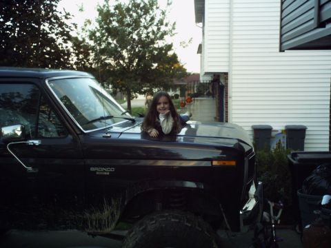 1986 Ford Bronco - A young girl rests on the hood of a black Ford Bronco, parked in a driveway.