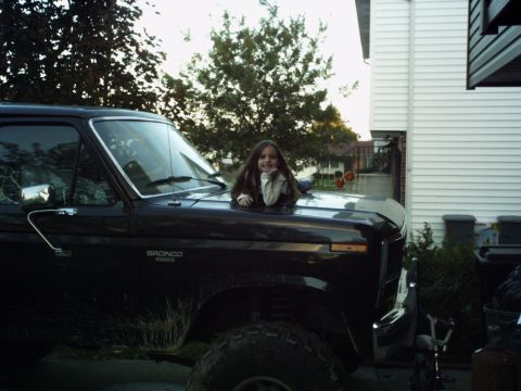 1986 Ford Bronco - A young girl poses on the hood of a black SUV, with the 'Bronco' nameplate visible on the fender.