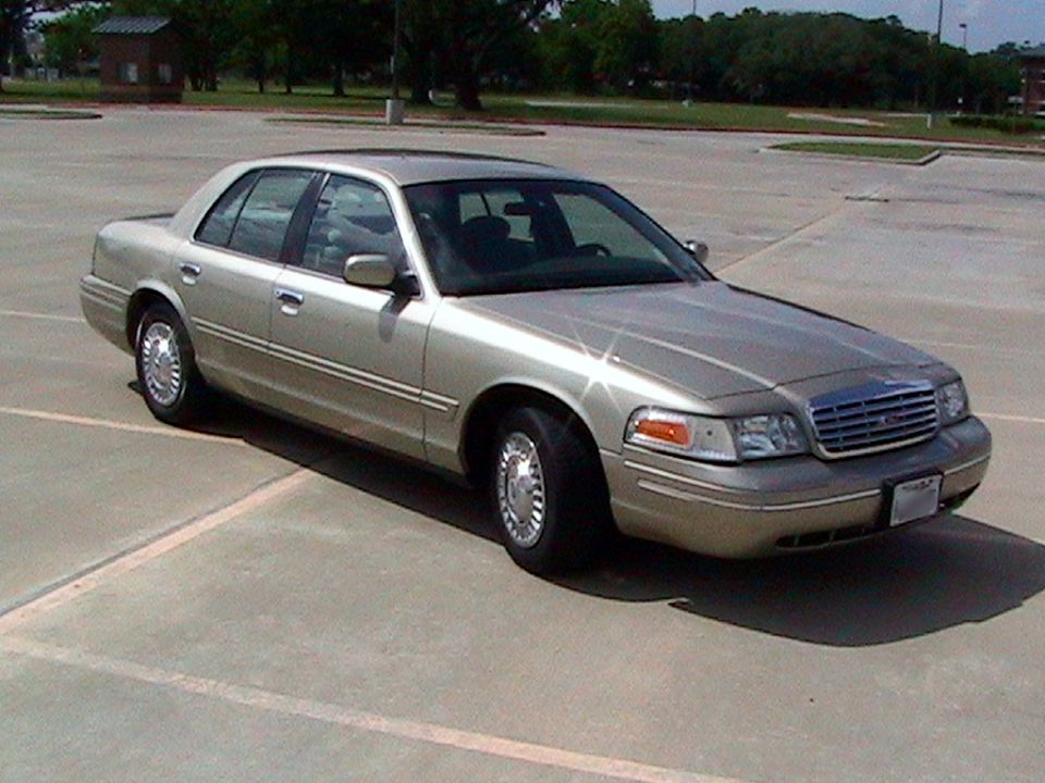 Gold Ford Crown Victoria sedan, front passenger 3/4 view, in an empty parking lot.