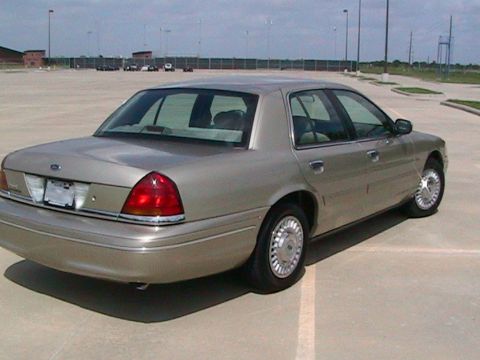 2000 Ford Crown Victoria - Rear three-quarter passenger-side view of a light gold Ford Crown Victoria sedan with factory lacy-spoke wheel covers and a Texas plate, pa…