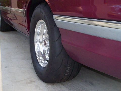 1992 Ford Crown Victoria - Close-up of the rear wheel of a maroon sedan on concrete, showing a very wide drag radial with a soft rounded sidewall mounted on a polishe…
