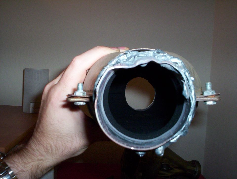 Hand holding a metal exhaust pipe with visible welds and bolt mounts