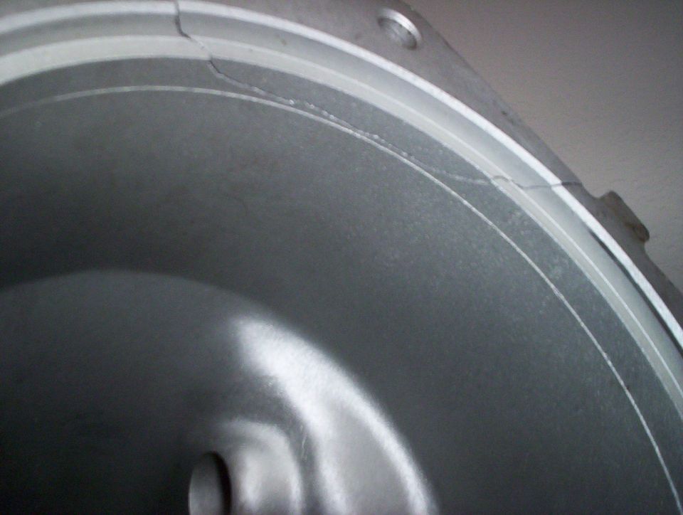 Cracked metal engine part, possibly a housing or cover, with a silver finish