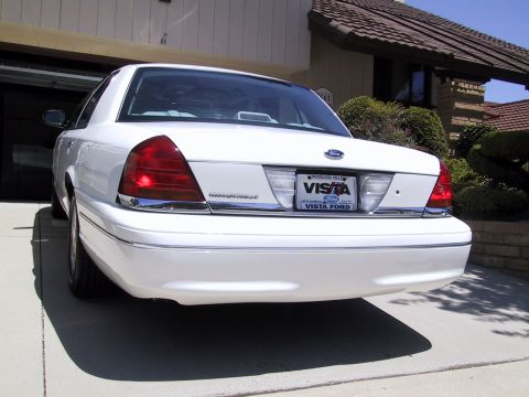 2003 Ford Crown Victoria - The rear of a white 2003 Ford Crown Victoria is visible, parked in front of a garage and house.