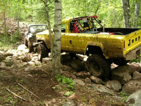 1977 Ford F-150 - Two off-road vehicles tackle a challenging rocky trail in a wooded area.