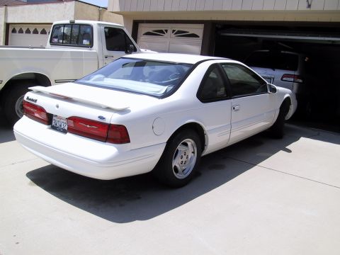 1997 Ford Thunderbird - A white 1997 Ford Thunderbird is parked in a driveway next to a white pickup truck.