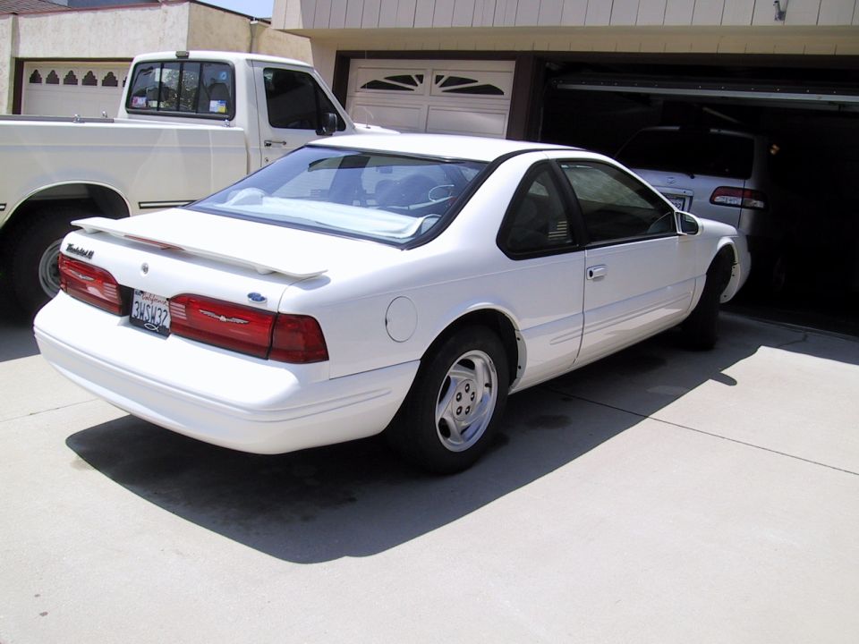 White 1997 Ford Thunderbird parked in front of a garage with a white pickup truck next to it