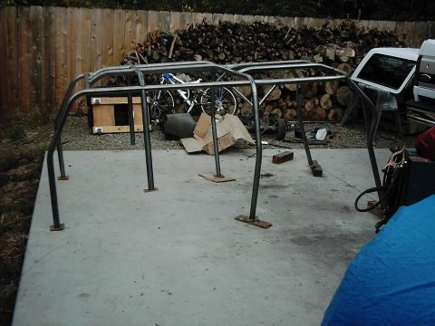 1978 Ford Bronco - A custom-fabricated roll cage sits on a concrete pad, with a woodpile and bicycle visible behind it.