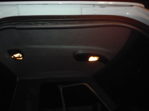 1978 Ford Bronco - The interior of a white vehicle shows two illuminated dome lights on the headliner.