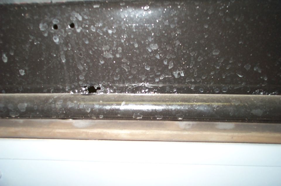 Close-up of water-spotted dark metal window frame and channel