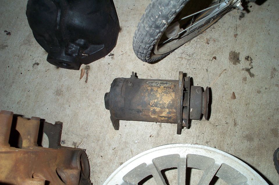 Rusty generator with pulley on concrete floor among other vehicle parts