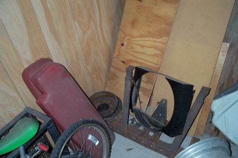 1954 Jeep Wrangler - A red seat and a fan shroud are stored indoors with other parts.