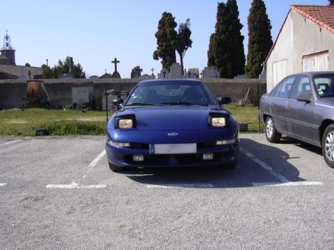 1994 Ford Probe - A blue Ford Probe is parked in a lot, with a cemetery in the background and another car beside it.