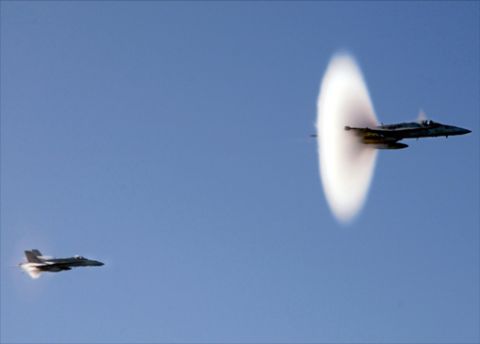 1987 Ford Bronco - Two fighter jets fly through a clear blue sky, with one jet generating a distinct sonic boom.