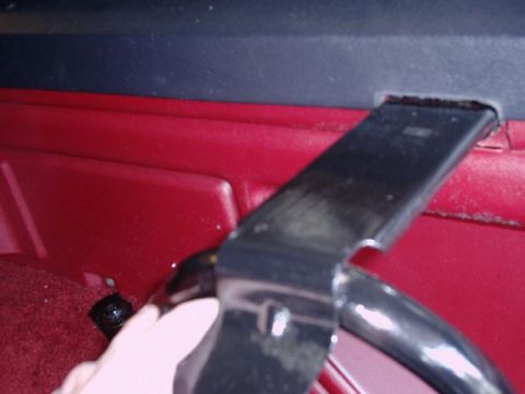 1984 Ford Bronco - A metal bracket is being fitted into the interior of a vehicle, near red upholstery and carpet.