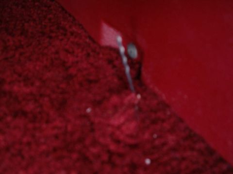 1984 Ford Bronco - Interior view of a red carpet and a red metal panel with a bolt.