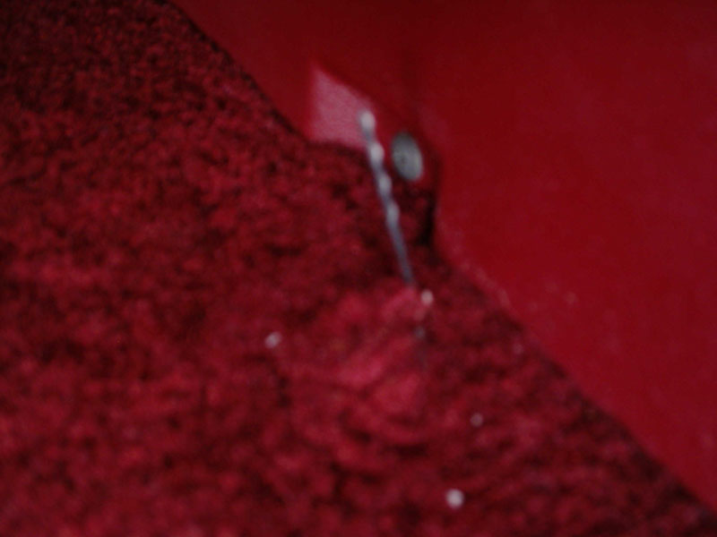 Blurry close-up of a small pilot hole drilled in a red painted panel beside red carpet
