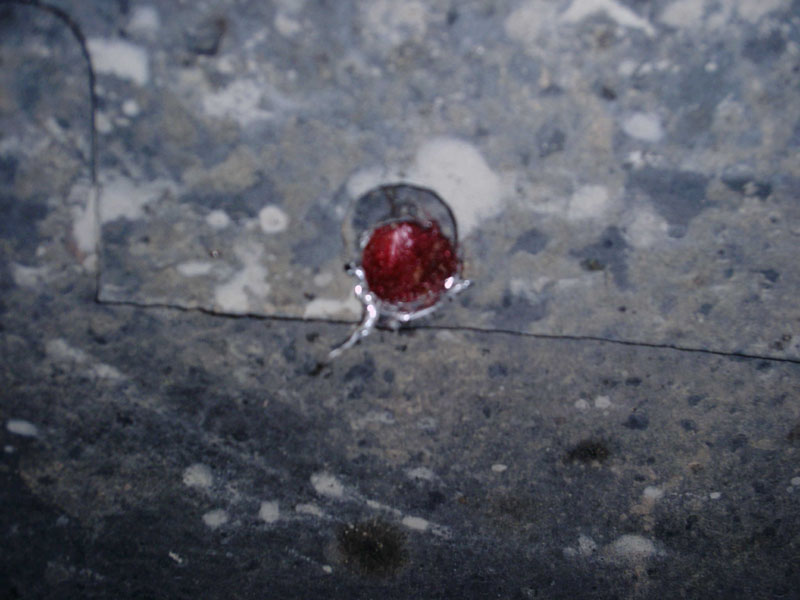 Freshly drilled hole in gray undercoated sheet metal showing red paint beneath