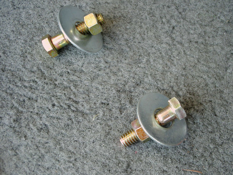 Two zinc-plated bolts with large fender washers and double hex nuts on gray carpet