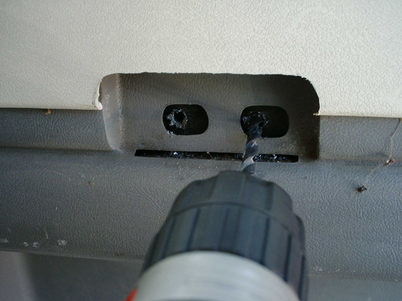 Drill boring pilot hole into gray plastic panel with recessed oval slots.