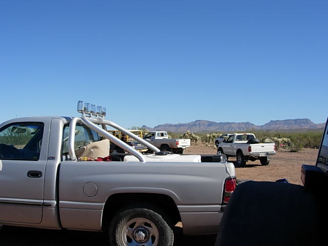 Several pickup trucks parked in a desert area with mountains in the background