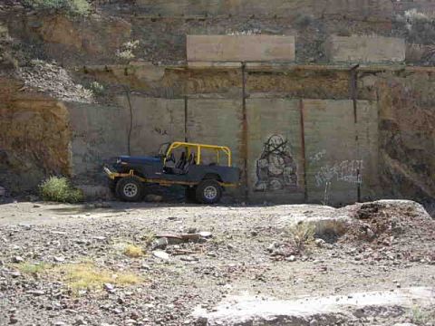 1981 Ford F-150 - A black off-road vehicle with a yellow roll cage sits on a dirt lot next to a graffiti-covered wall.