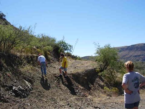 1981 Ford F-150 - Several people are seen walking along a dirt path in a dry, mountainous terrain under a clear blue sky.