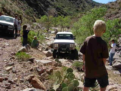 1981 Ford F-150 - People and off-road vehicles navigate a , rocky trail in a mountainous, arid environment.
