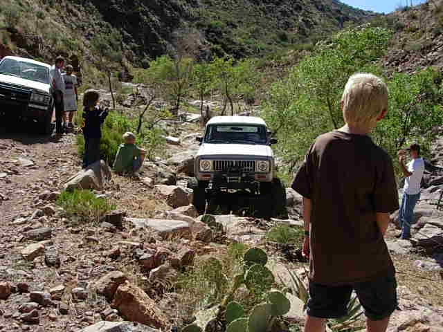 Two off-road vehicles on a rocky trail with people watching