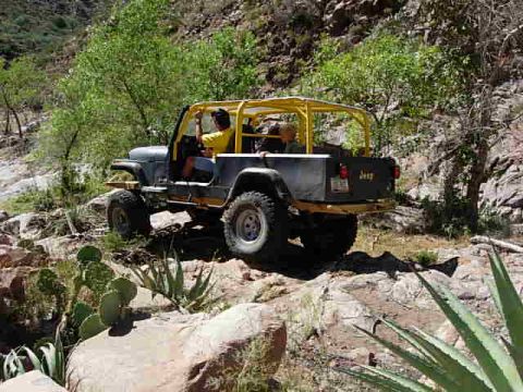 1981 Ford F-150 - A gray Jeep CJ-7 with a yellow roll cage navigates a , rocky terrain.