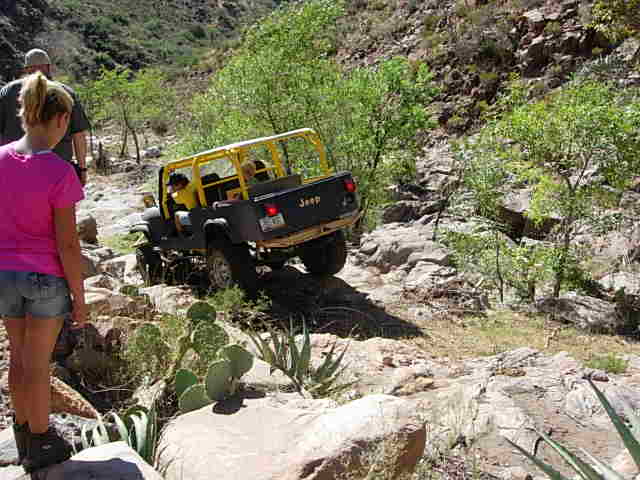 Yellow roll cage on black Jeep CJ-7 navigating rocky terrain