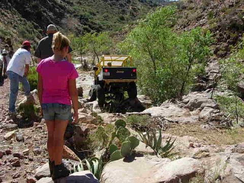 1981 Ford F-150 - A group of people and a Jeep Wrangler navigate a rough, rocky off-road trail in a desert canyon.