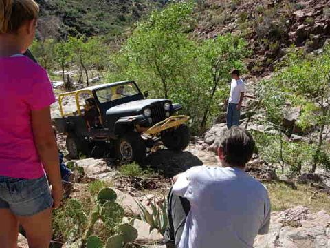 1981 Ford F-150 - A group of people observe a black Jeep CJ-7 navigating a rocky, off-road trail.