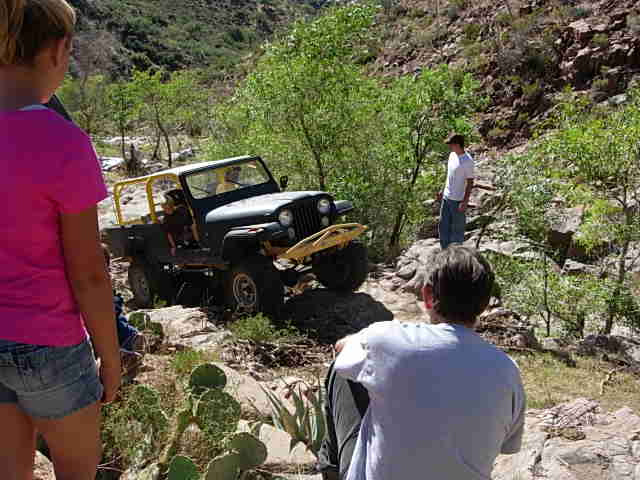 Black Jeep CJ-7 with yellow roll cage on rocky terrain