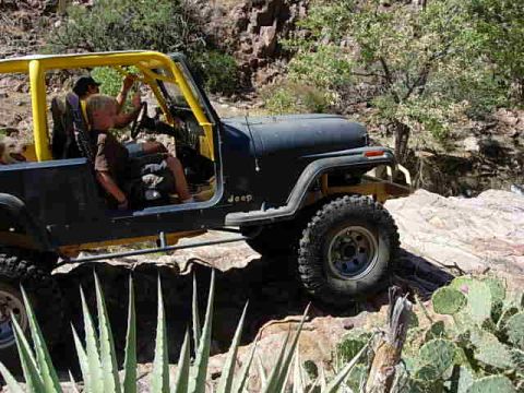 1981 Ford F-150 - A black Jeep CJ-7 with a yellow roll cage navigates a rocky trail, with two people inside.