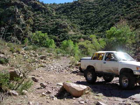 1981 Ford F-150 - A white pickup truck navigates a rough dirt road through a scenic, hilly landscape.
