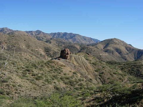 1981 Ford F-150 - A vast desert landscape unfolds under a clear blue sky, rolling hills and a striking rock outcrop.