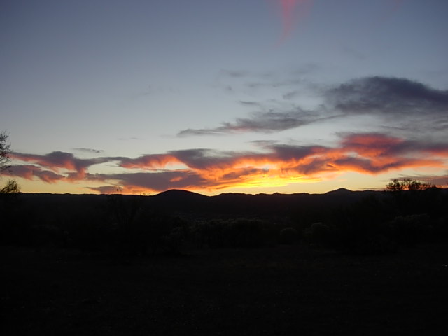 Sunset with orange and pink clouds over dark hills and silhouetted trees