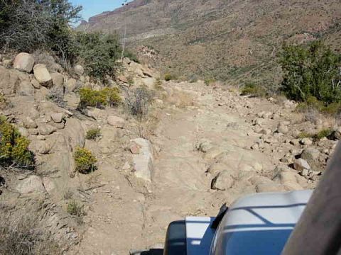 1981 Ford F-150 - The vehicle is on a rough, rocky path in a dry, mountainous area. The text 'SUPERMOTORS' is visible on the vehicle.