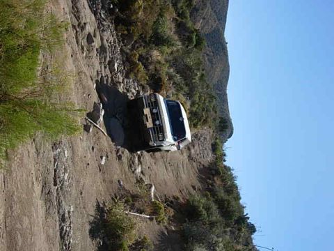 1981 Ford F-150 - A white pickup truck navigates a precarious, narrow dirt path on a mountainside.